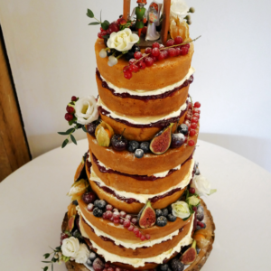 A three tier naked wedding cake, decorated with figs, blueberries and raspberries as well as flowers. Topped with a Disney's Robin Hood cake topper.